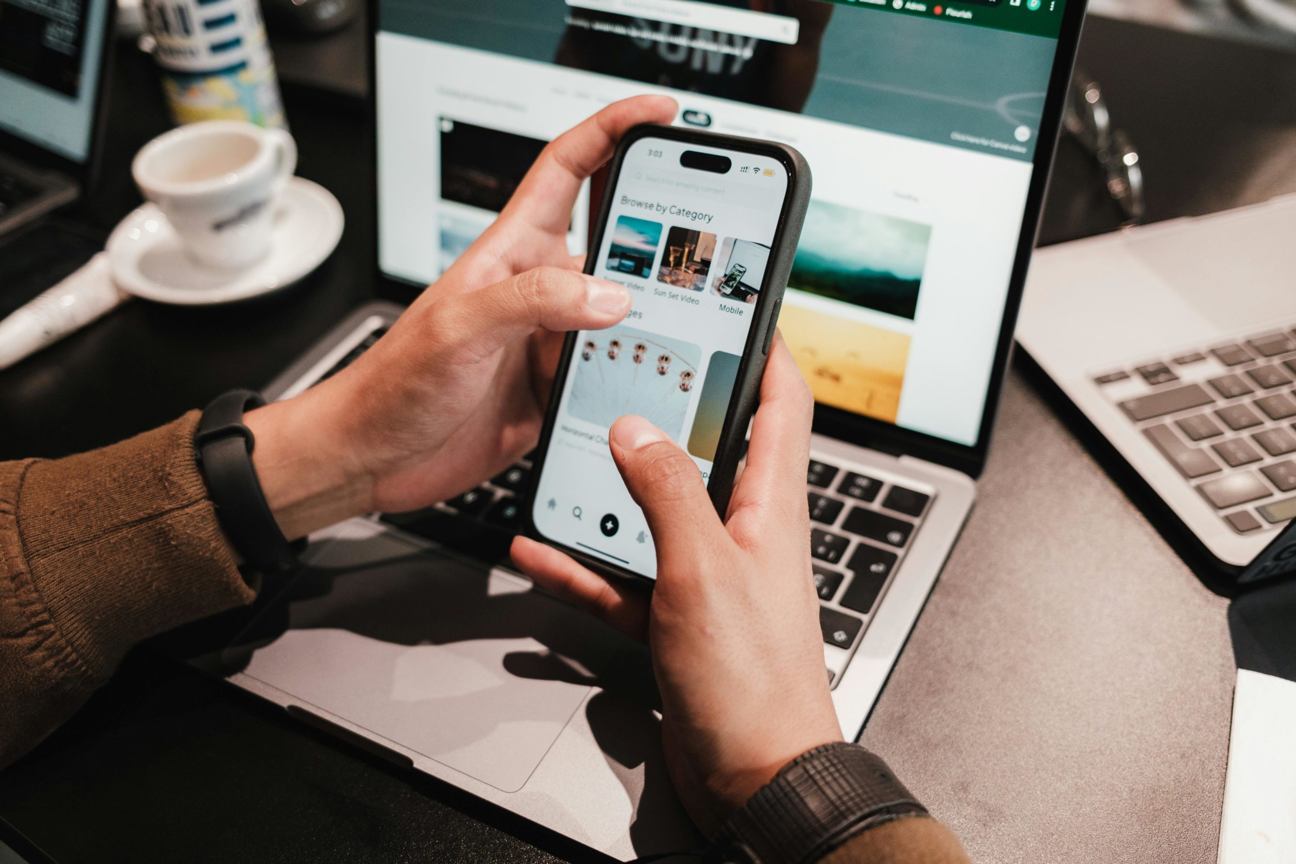 Eine Person hält ein Smartphone in der Hand und hat einen Laptop vor sich. Darstellung der Frage, wie es Unternehmen schaffen, aus der Content-Flut herauszustechen.